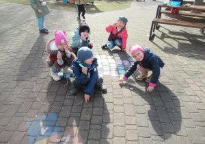 Dzieci rysują kredą w ogródku przedszkolnym.
