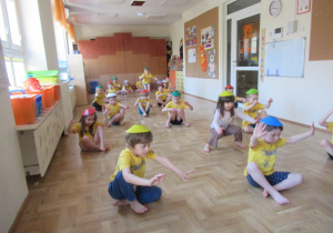 Dzieci siedzą na podłodze, na ich głowach kolorowe krążki.