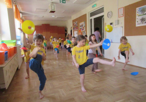 Dzieci kopią w kolorowe krążki podczas zajęć gimnastycznych z elementami taekwondo.