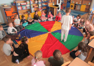 Dzieci siedzą wokół chusty animacyjnej, jeden chłopiec stoi na chuście.