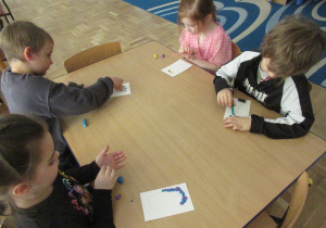 Dzieci przy stoliku wyklejają plasteliną litery c.