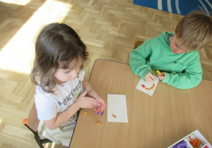 Chłopiec i dziewczynka siedzą przy stoliku i wyklejają literę c kolorową plasteliną.