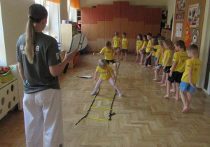 Dzieci ćwiczą z użyciem drabinki koordynacyjnej.