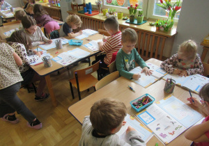 Dzieci przy stolikach pracują w książkach.