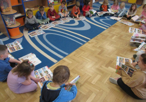 Dzieci siedzą w kole i oglądają książki.