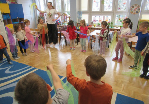 Dzieci stoją w kole trzymając w ręach kolorowe chustki.