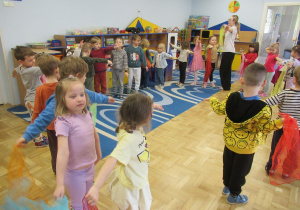 Dzieci maszerują w kole trzymając w rękach kolorowe chustki,