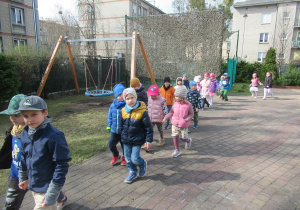 Dzieci maszerują w parach w ogródku przedszkolnym.