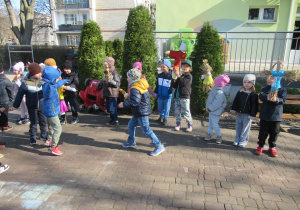 Dzieci stoją z Marzannami w ogrodzie przedszkolnym.