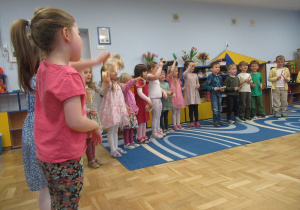 Dzieci stoją w półkolu podczas miniwystępu podczas warsztatów wiosenno - wielkanocnych.