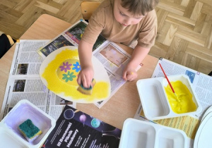 Chłopiec maluje pisankę wyciętą z papieru