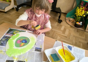 Dziewczynka maluje pisankę wyciętą z papieru