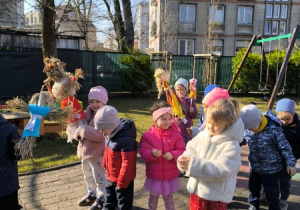 Dzieci spacerują po ogrodzie przedszkolnym z Marzannami