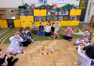 Dzieci siedzą w kręgu wokół trójkąta ułożonego z trójkątnych klocków