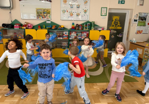 Dzieci tańczą z niebieskimi pomponami - interpretują ruchem utwór "Wiosna" autorstwa Antoniego Vivaldiego