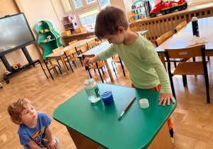 Chłopiec - za pomocą pipety - umieszcza niebieski płyn w słoiku wypełnionym wodą i pianką do golenia