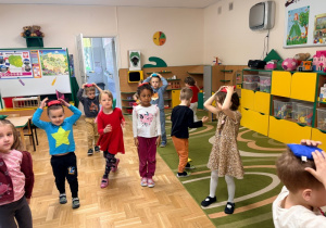 Dzieci chodzą po sali z woreczkami gimnastycznymi na głowie