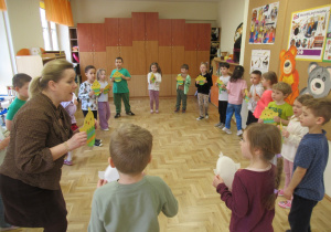Dzieci stoją w kole podczas rytmiki, trzymają w rękach kurczaczki z papierowych talerzyków.