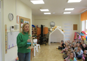Pani prezentuje dzieciom wagę, dzieci siedzą na podłodze.