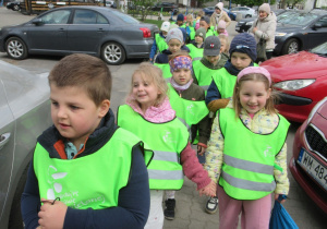 Dzieci idą w parach w ofblaskowych kamizelkach.
