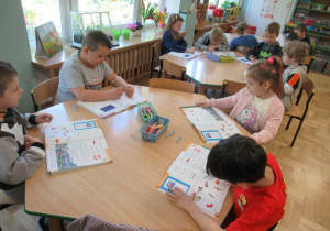 Dzieci siedzą przy stolikach i pracują w książkach.