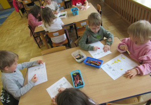 Dzieci siedzą przy stolikach i kolorują.