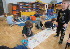 Chłopcy kolorują kolorowankę rozłożoną na podłodze.