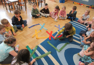 Dzieci siedzą w kole, w środku ułożone litery Ł z szarf.