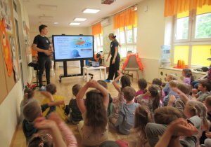 Dzieci siedzą na podłodze przed monitorem podczas warsztatów "Bezpieczeństwo nad wodą".