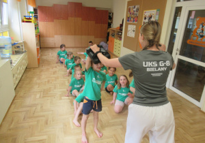 Dzieci siedzą w dwóch rzędach podczas zajęc z elementami taekwondo.