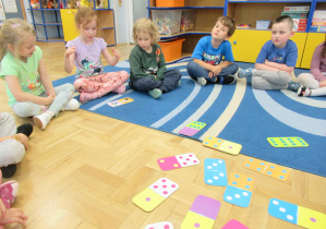 Dzieci siedzą na dywanie podczas zajęć, przed nimi tabliczki domino.