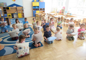 Dzieci siedzą w sali i trzymają w rękach poduszeczki.