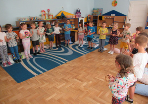 Dzieci stoja w półkolu i grają na instrumentach.