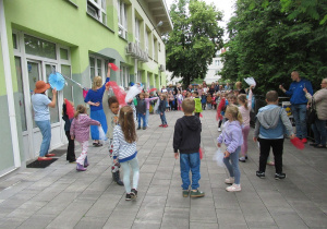 Dzieci stoją w kole i wymachują białymi i czerwonymi chusteczkami.