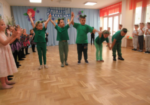 Dzieci stoją w półkolu i klaszczą, na środku kłaniają się dzieci w strojach żab.