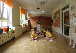 Dzieci siedzą w dwóch rzędach podczas zajęć z elementami taekwondo.