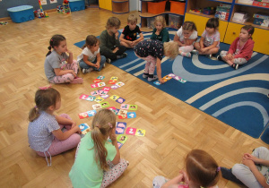 Dzieci siedzą w kole i grają w domino.