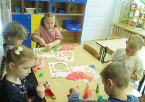 Dzieci przy stoliku wykonują prace plastyczne.