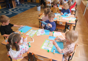 Dzieci przy stolikach wkonują prace plastyczne.