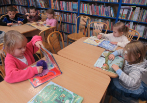 Dzieci w bibliotece oglądają ksążki.