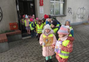 Dzieci wychodzą z biblioteki, dwie dziewczynki trzymają wypożyczone książki.