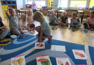 Dzieci siedzą na dywanie podczas zajęć, dziewczynka pokazuje literkę "o" na obrazku.