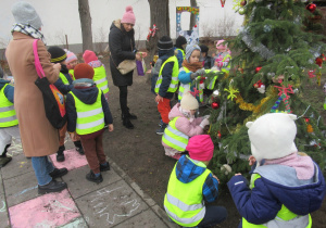 Dzieci dekorują choinkę w ogródku przy Ośrodku Wsparcia dla Seniorów.