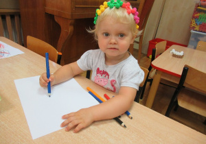 Dziewczynka siedzi przy stoliku i rysuje.