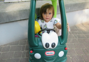 Dziewczynka siedzi w zielonym samochodziku.