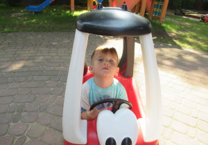 Chłopiec jeździ w plastikowym samochodziku.
