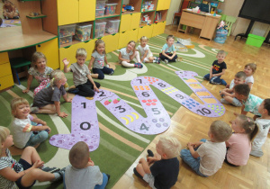 Dzieci siedzą w kole na dywanie, przed nimi ułożone puzzle w kształcie węża.