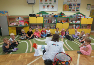 Dzieci siedzą na dywanie w półkolu podczas wasztatów LaboOdkrywców.