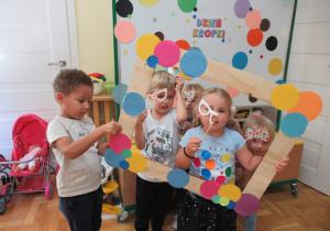 Dzieci pozują do zdjęcia trzymając ramkę w kolorowe kropki.