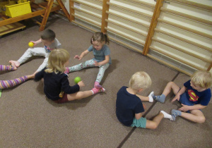 Dzieci siedzą na dywanie i turlają do siebie piłeczki.